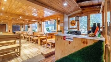 Interior de madera con bancos y mesas de madera, una recepción y vistas al exterior.