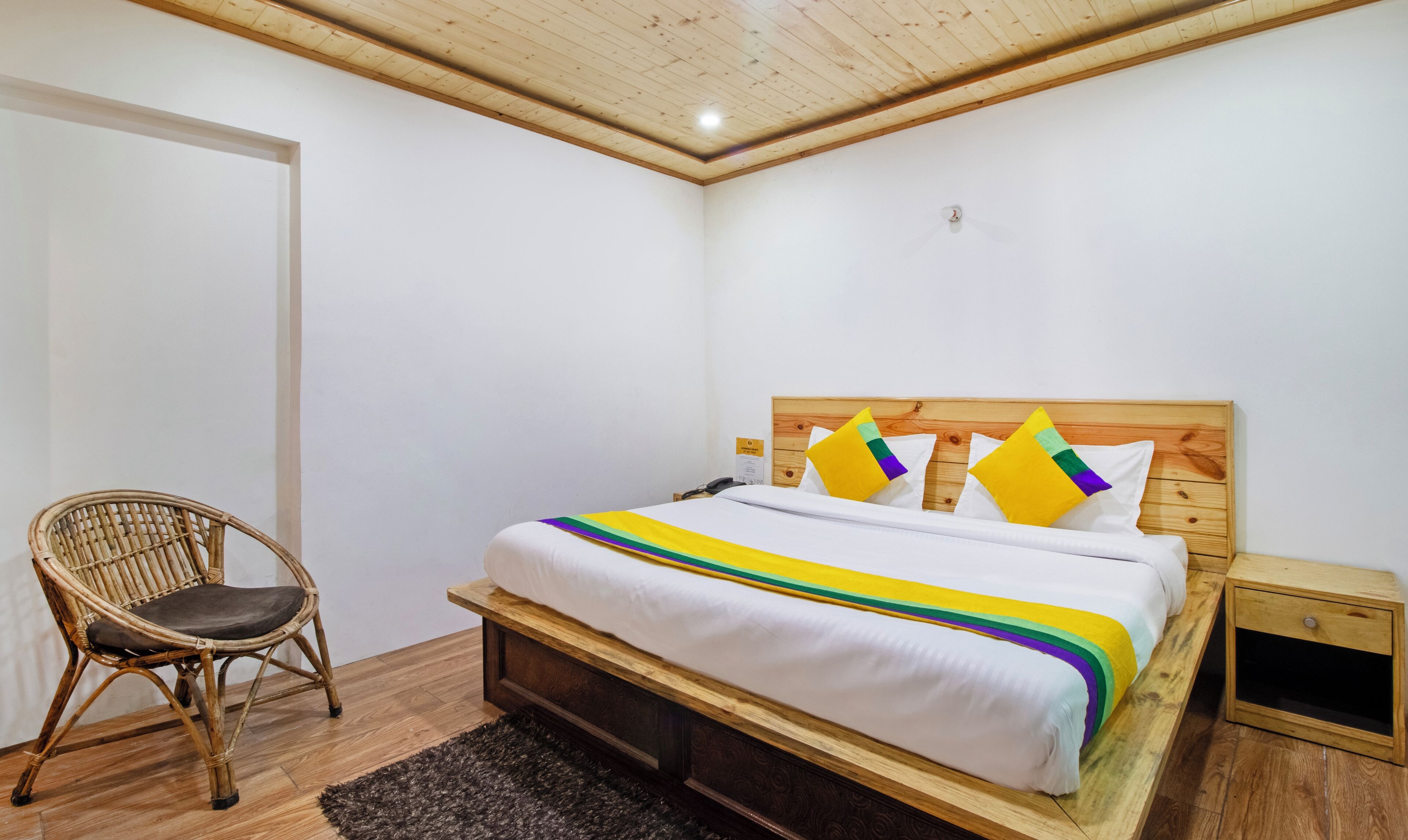 Een slaapkamer met een houten bed, een rieten stoel en een klein nachtkastje.