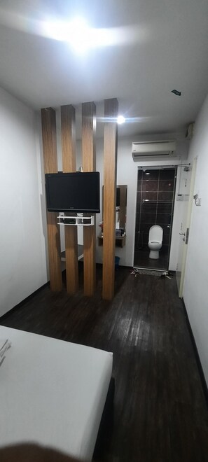 A hotel room with a TV mounted on a wooden partition, a shower area with a glass door, and a white toilet. - OYO 90724 Rg Hotel (Ayer Hitam)