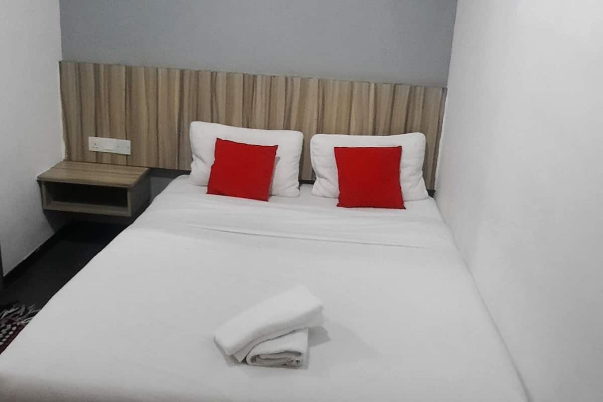 A neatly made bed with white and red pillows, a wooden nightstand, and a wall-mounted light fixture.