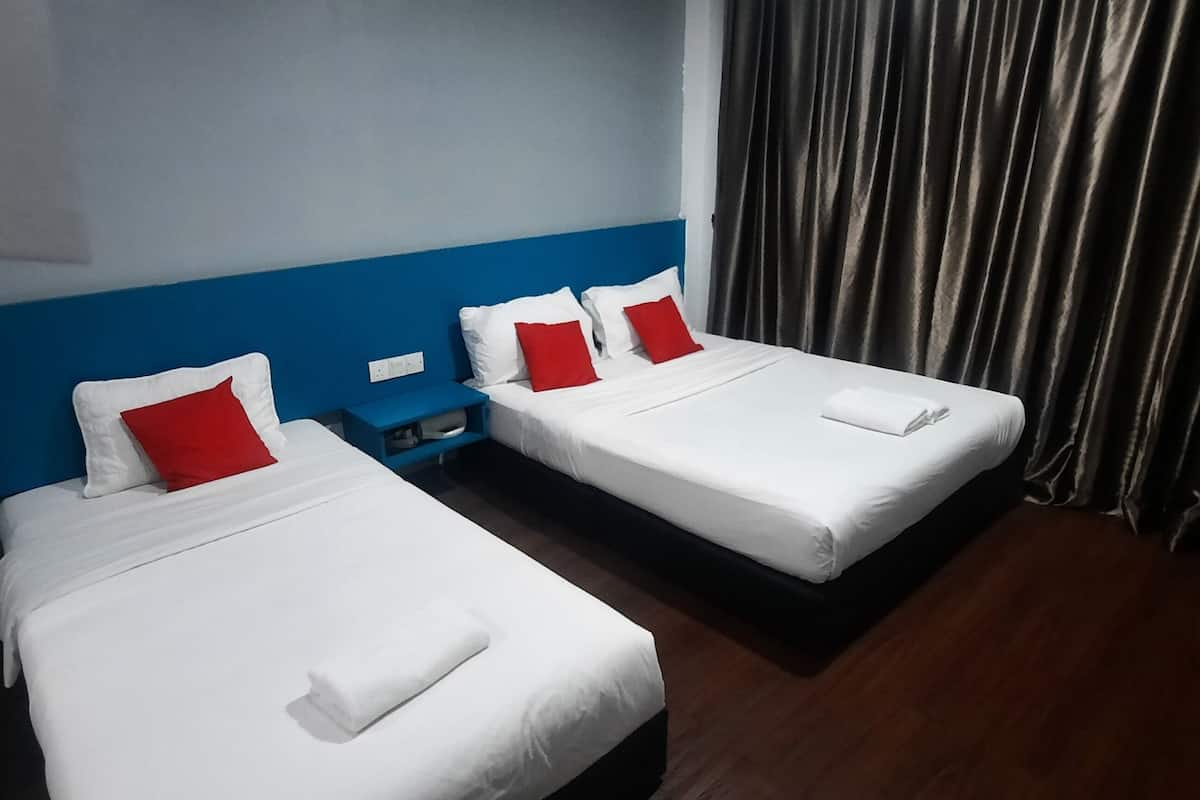 Two single beds with white bedding and red pillows, a blue headboard, a nightstand, and a dark curtain.
