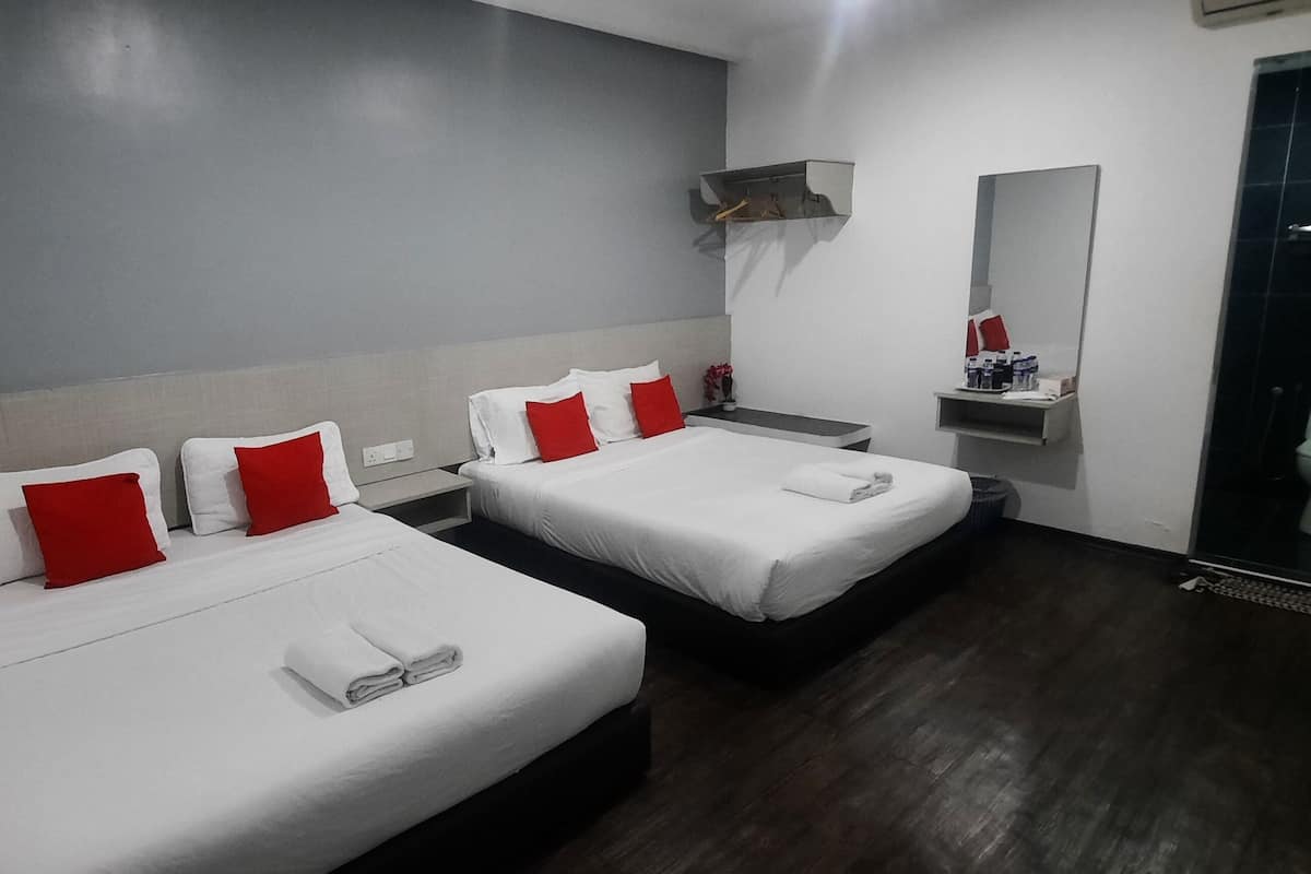 A hotel room with two beds, each with white linens and red pillows, a small bedside table, a mirror, and a shower area.