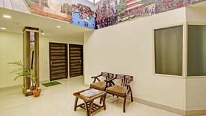 Un hall d’entrée avec un comptoir de réception, deux portes en bois, un espace détente avec deux fauteuils et une table, et une grande fenêtre.