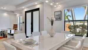 A modern dining area with a large white table set for four, surrounded by white chairs. - Lynora`s Luxe Estate - 3BR/3BA w/ Modern Design & Heated Pool (Fort Lauderdale)