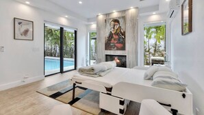 A modern bedroom with a large bed, a fireplace, and a view of a swimming pool. - Lynora`s Luxe Estate - 3BR/3BA w/ Modern Design & Heated Pool (Fort Lauderdale)