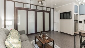 Un saló modern amb un sofà, una taula de centre amb objectes decoratius, una televisió i una zona de cuina amb armaris i electrodomèstics.