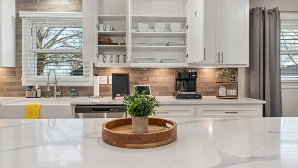 Una cocina moderna con armarios blancos, una cafetera y una planta en la encimera.