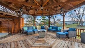 Una terraza techada al aire libre con piso de madera, asientos acolchados azules y ventiladores de techo.