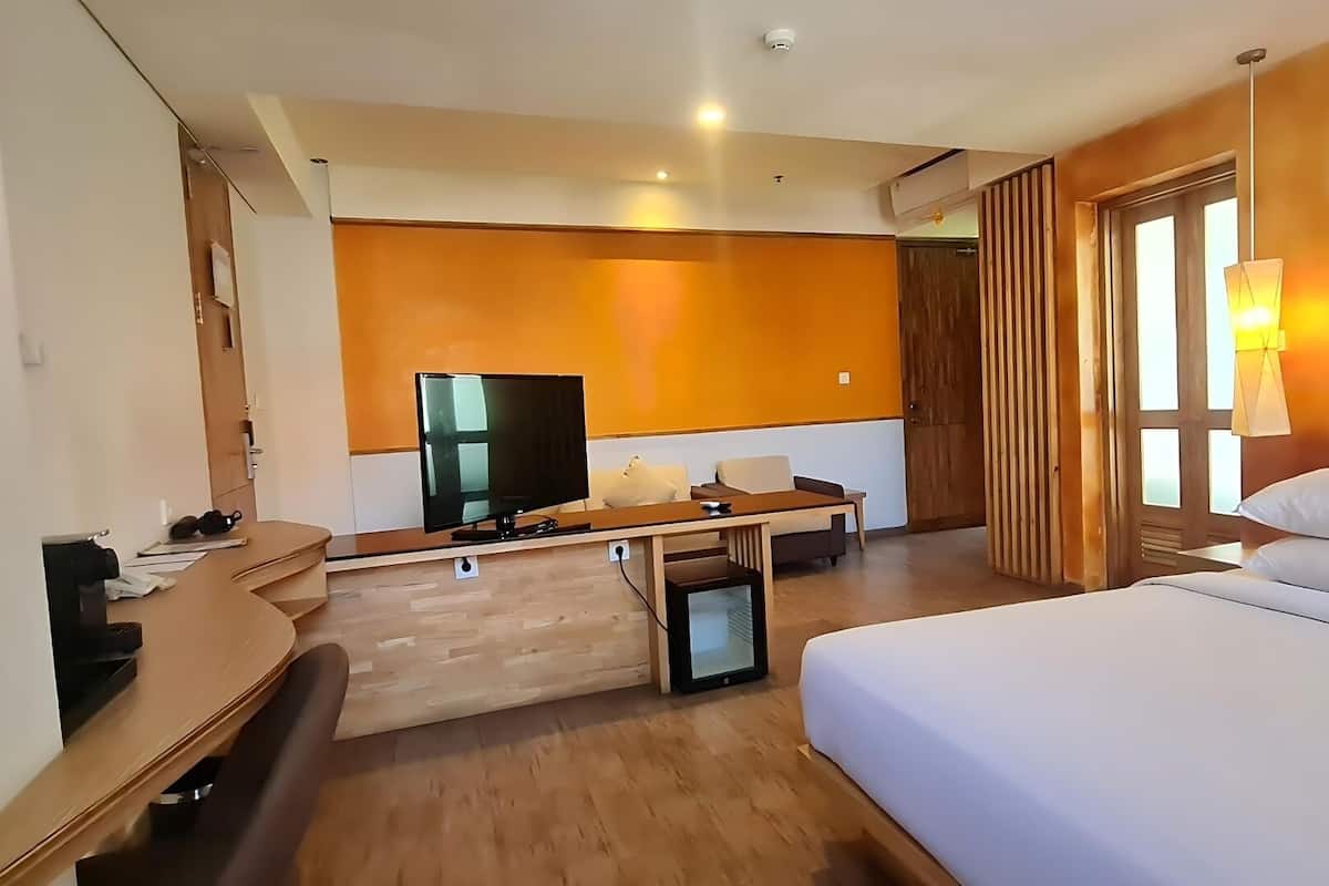 Une chambre d’hôtel comprenant un lit, un bureau avec un téléviseur à écran plat, un canapé et une fenêtre avec des rideaux.