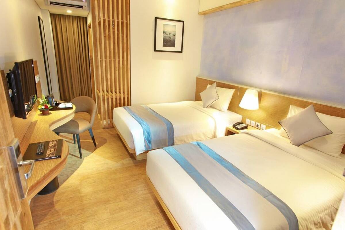 Une chambre d’hôtel avec deux lits, un bureau avec une chaise, une télévision et une fenêtre avec des rideaux.