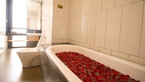 A modern bathroom with a bathtub filled with rose petals, a toilet, and a sink. - Liberta Hotel Jimbaran (Kedonganan)