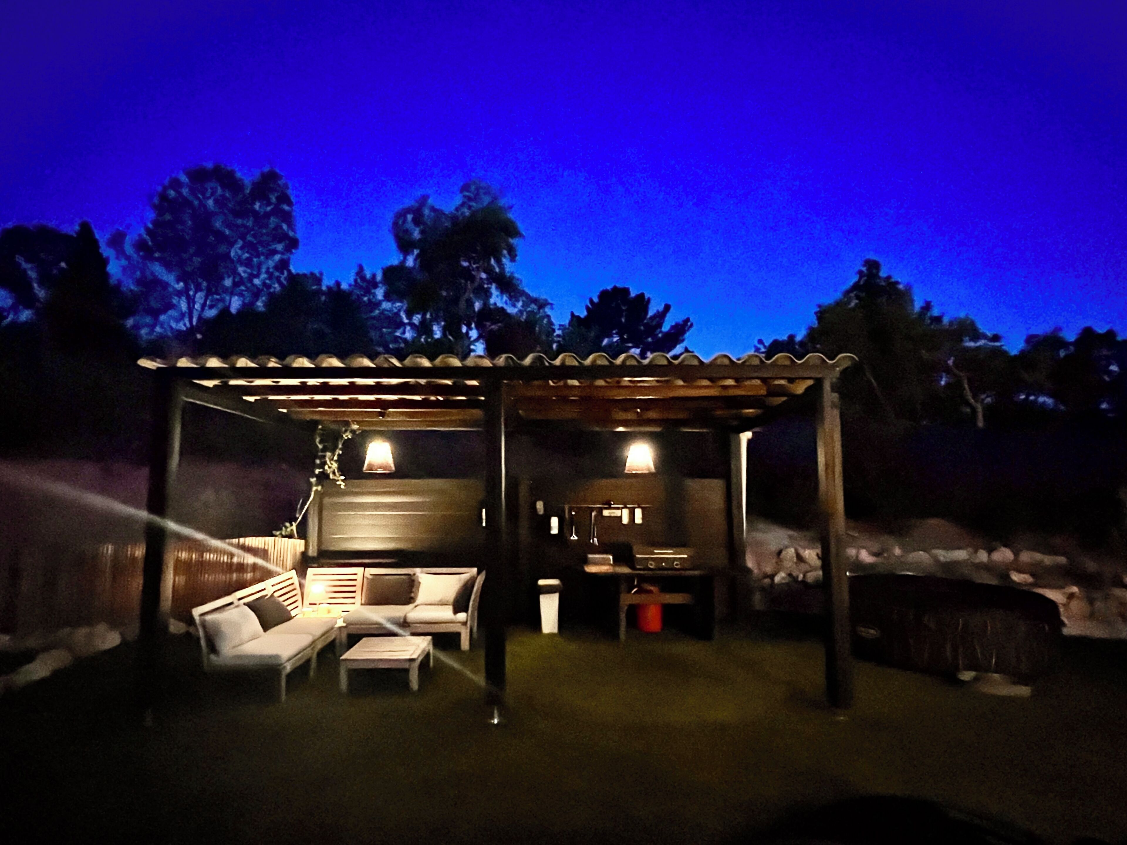 An outdoor patio area with a covered seating area, a small table, and a trash bin.