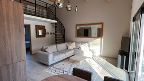 Un salon moderne doté d’un grand canapé d’angle, d’une table à manger en bois et d’un escalier menant à un niveau supérieur.