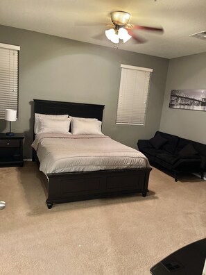 Une chambre à coucher avec un lit, une table de chevet, un canapé noir et un ventilateur de plafond.