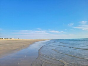 A beach with a clear sky, calm water, and distant buildings.