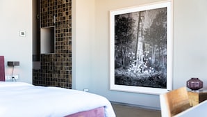 A modern hotel room with a large bed, a wooden bench, a tiled wall, and a framed forest photograph. - Hotel Piet Hein Eek (Eindhoven)