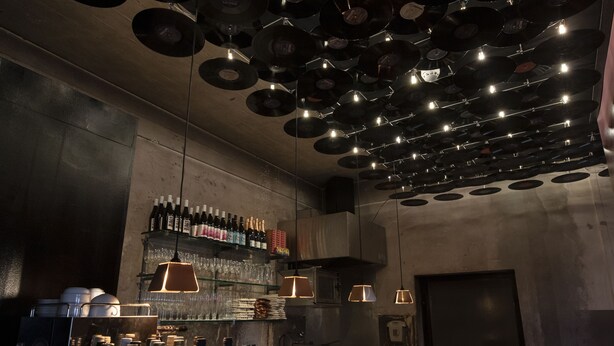 A bar area with shelves of bottles, glasses, and a ceiling adorned with vinyl records. - Hotel Piet Hein Eek (Eindhoven)