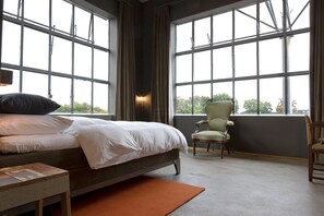 Un dormitorio con una cama grande, una silla y vistas amplias a través de grandes ventanales.