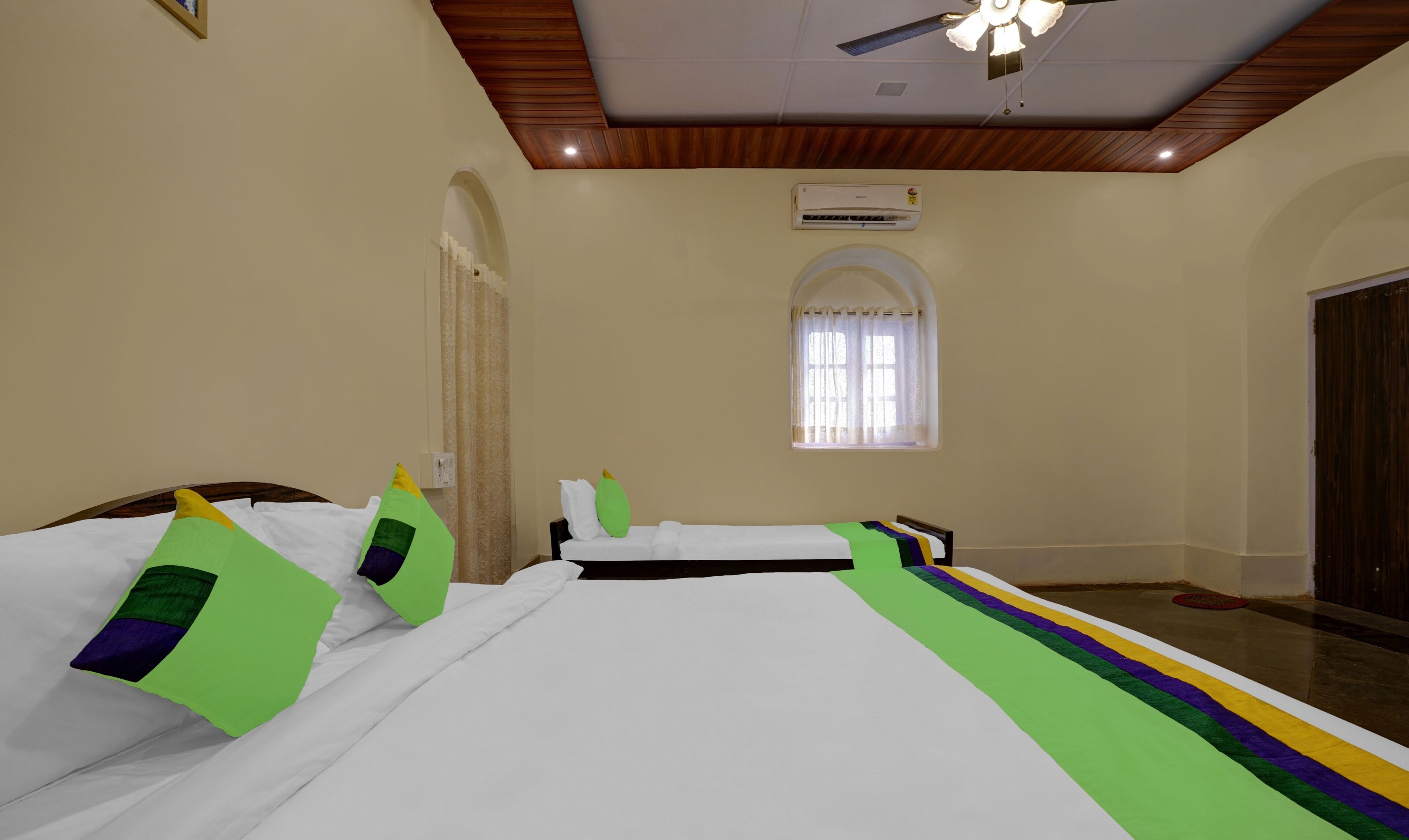 A hotel room with two beds, a ceiling fan, an air conditioning unit, and a window with curtains.