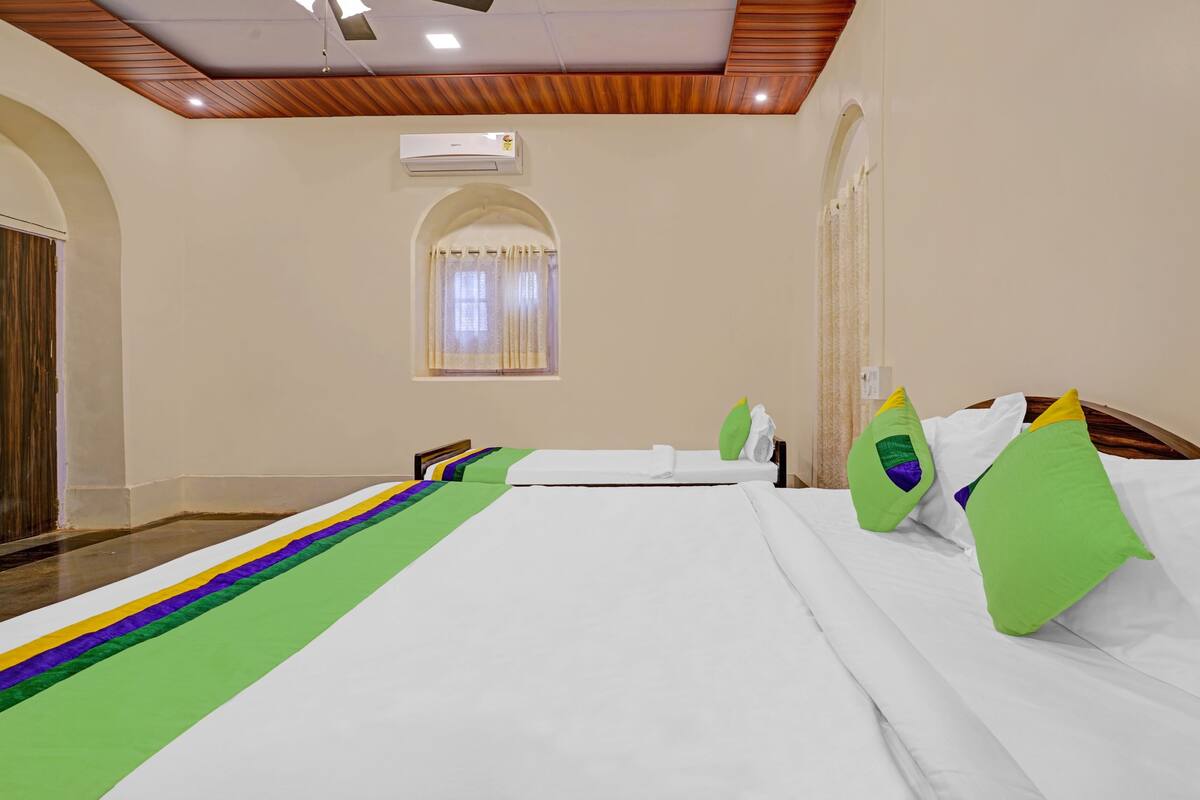 Habitación de hotel con una cama grande, techo de madera, unidad de aire acondicionado y ventana con cortinas.