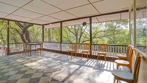 A covered outdoor area with a checkered floor, wooden chairs, a table, and a view of trees through large windows. - Treebo Cecil Resort Matheran (Karjat)