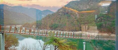 A suspension bridge over a river with a mountainous backdrop.