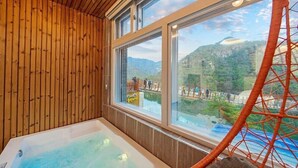Une pièce en bois avec une grande fenêtre, un jacuzzi et une vue sur une région montagneuse.