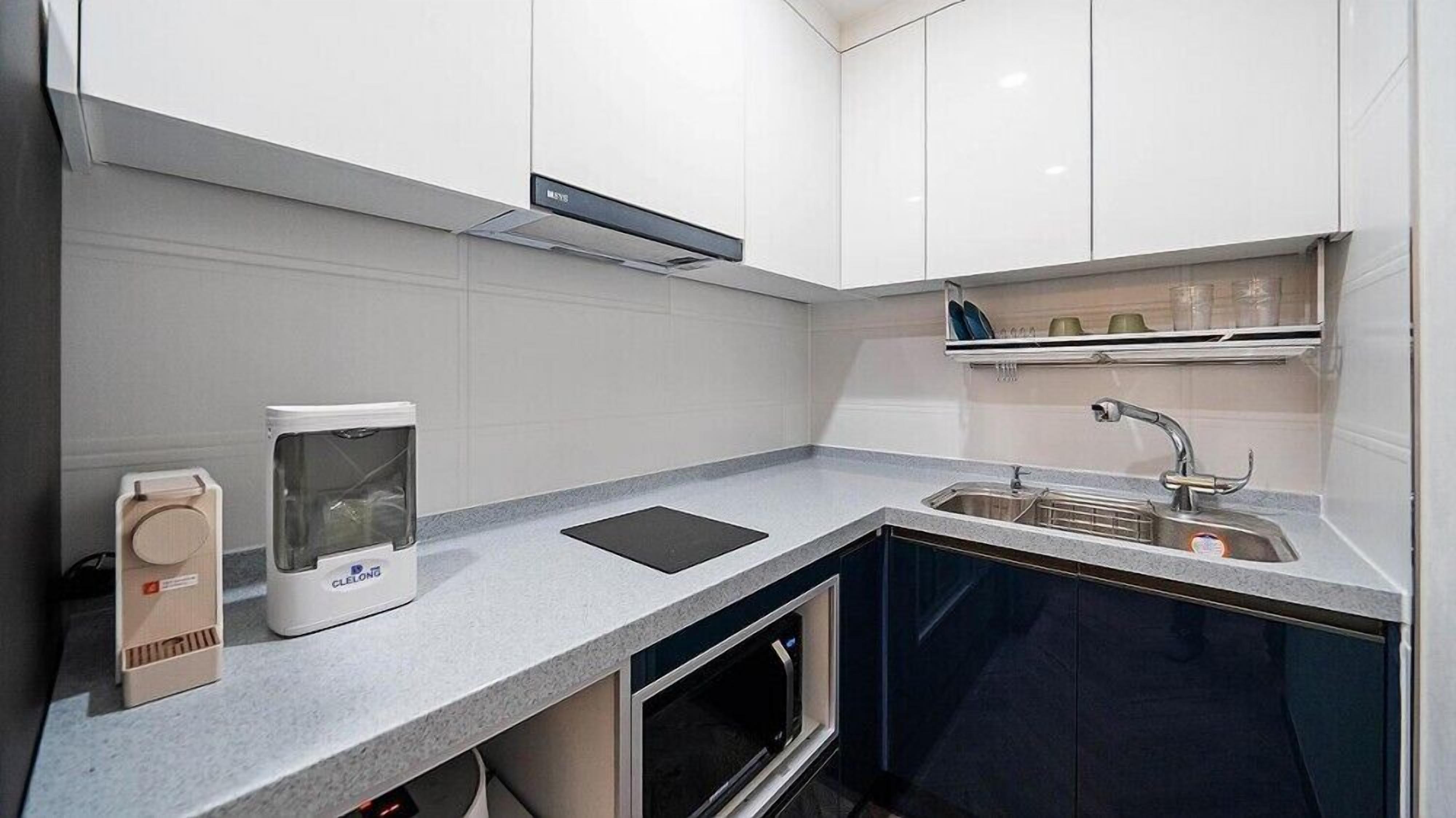 Una cocina moderna con armarios blancos, un lavamanos de acero inoxidable, horno empotrado y un refrigerador compacto.
