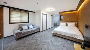 Une chambre d’hôtel moderne avec un canapé gris, un grand lit, des panneaux de bois et un parquet à motifs en chevrons.