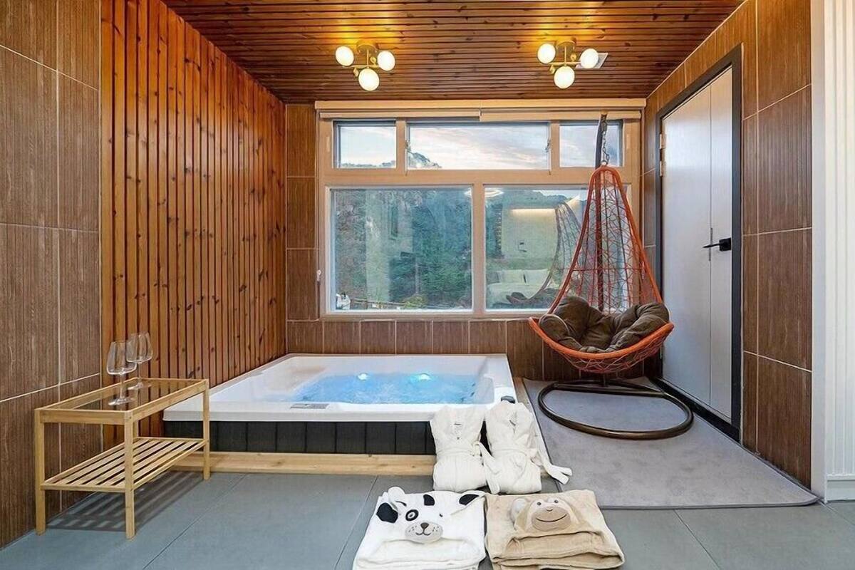 A modern bathroom with a wooden interior, a large window, a hanging chair, a bathtub, and towels.