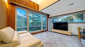 Un salon moderne avec un canapé, un téléviseur à écran plat et de grandes fenêtres donnant sur l’extérieur.