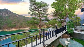 Un balcon avec vue sur une rivière et des montagnes, aménagé avec des fauteuils et une table en osier.