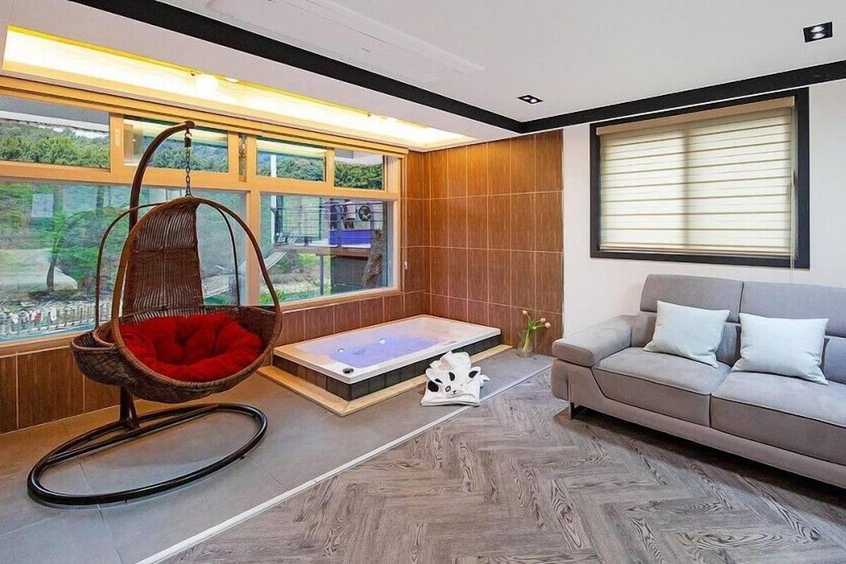 A modern room with a hanging chair, a sofa, a bathtub, and large windows.