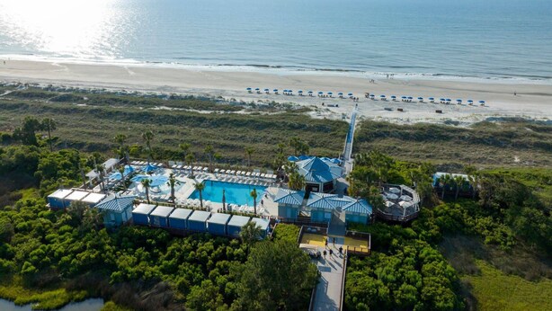 Eine Vogelperspektive auf ein Resort mit Pool, Strandstühlen und Strand.