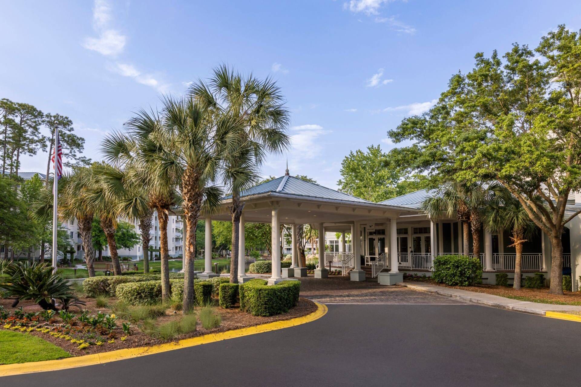 A covered pavilion with a roof, surrounded by palm trees and a well-maintained garden.