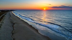 A beach at sunset with the sun setting over the ocean.
