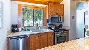 Eine Küche mit Holzausbau, Edelstahlgeräten, einer Arbeitsplatte aus Granit und einem Fenster mit Blick auf Bäume.