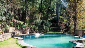 A swimming pool with a stone wall and lush greenery surrounding it. - Samarkand House (Samli)