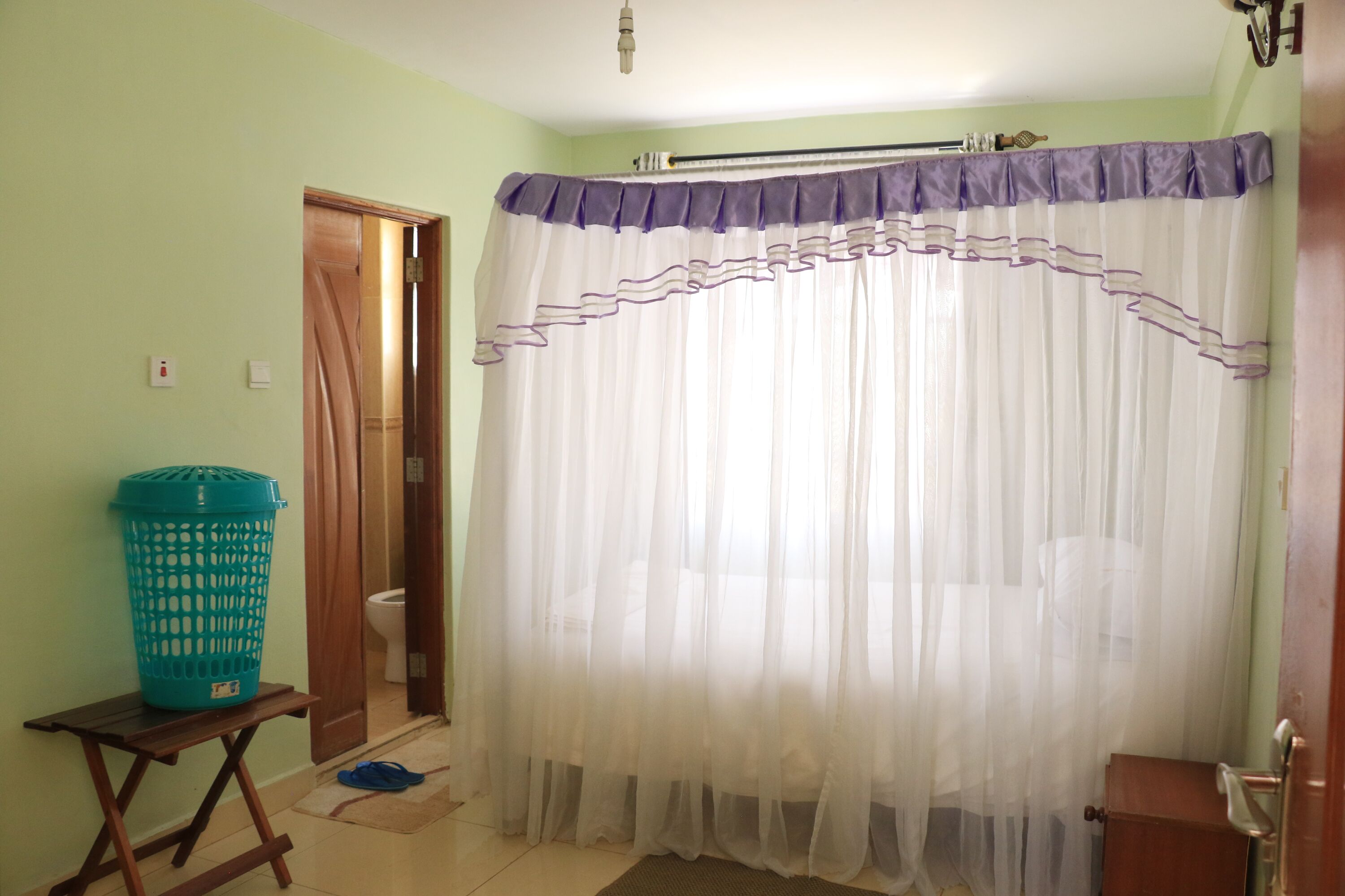 A bathroom with a shower curtain, a green laundry basket, and a wooden bench.