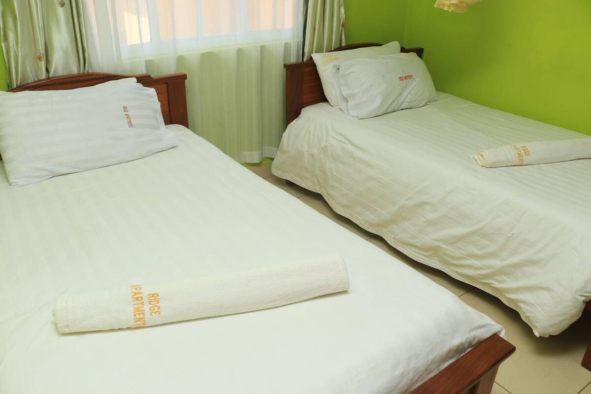 Two single beds with white linens and pillows, a wooden headboard, and a green wall.