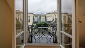 En balkon med et bord og stole, en potteplante og udsigt til omkringliggende bygninger.
