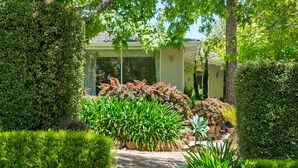 A house with a stone staircase leading to a covered porch, surrounded by lush greenery and a well-maintained garden. - Forest View House (Stirling)