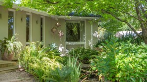 A house with a covered porch, surrounded by lush greenery and a gravel pathway. - Forest View House (Stirling)
