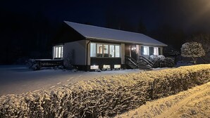 Une maison recouverte de neige, avec un toit en pente et un porche à l’avant.