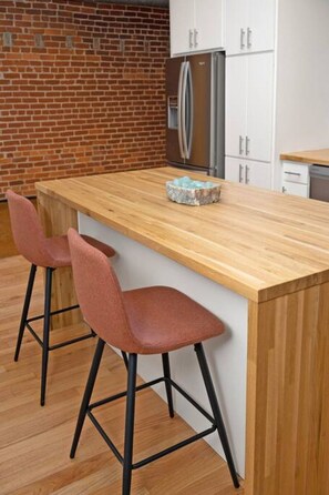 A kitchen with a wooden island, two bar stools, a refrigerator, and white cabinets. - Deluxe 3BR Loft Walkable to Everything Downtown (Cincinnati)
