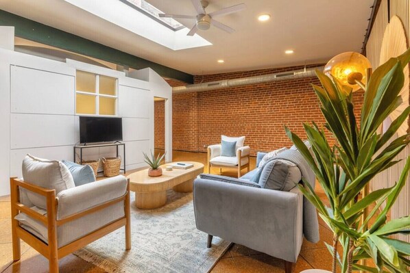 A modern living room with a TV, seating, and a brick wall. - Deluxe 3BR Loft Walkable to Everything Downtown (Cincinnati)