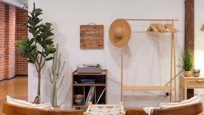 Une pièce avec une chaise et une table en bois disposées au centre, une plante, un chapeau posé sur un présentoir, et une étagère avec des livres et une petite plante.