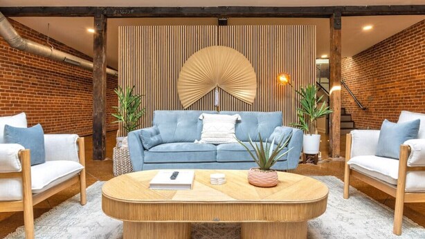 Un salon moderne avec un canapé bleu, deux fauteuils blancs, une table basse ronde en bois et un éventail décoratif.