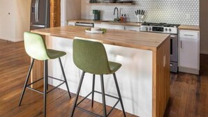Une cuisine moderne avec des poutres apparentes en bois, un grand îlot central doté de tabourets de bar et un réfrigérateur en acier inoxydable.