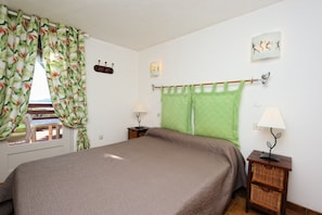A bedroom with a bed, two bedside tables, a window with curtains, and wall art.